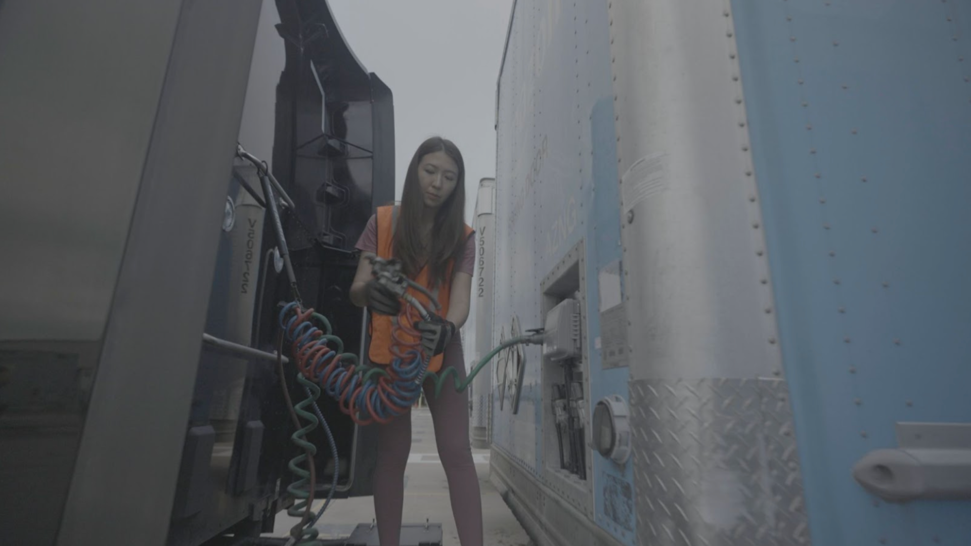 A woman connecting air brake lines between a truck cab and its trailer.