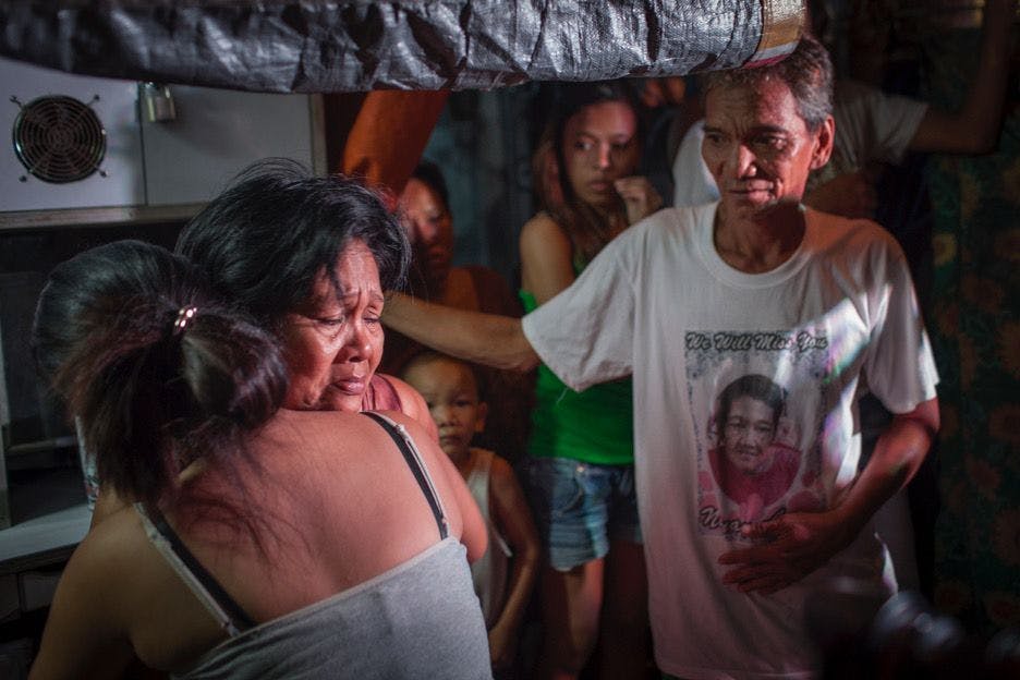 An elderly woman is comforted by her relatives after witnessing her son dead on the pavement in a dark alley in Tondo, Manila.
