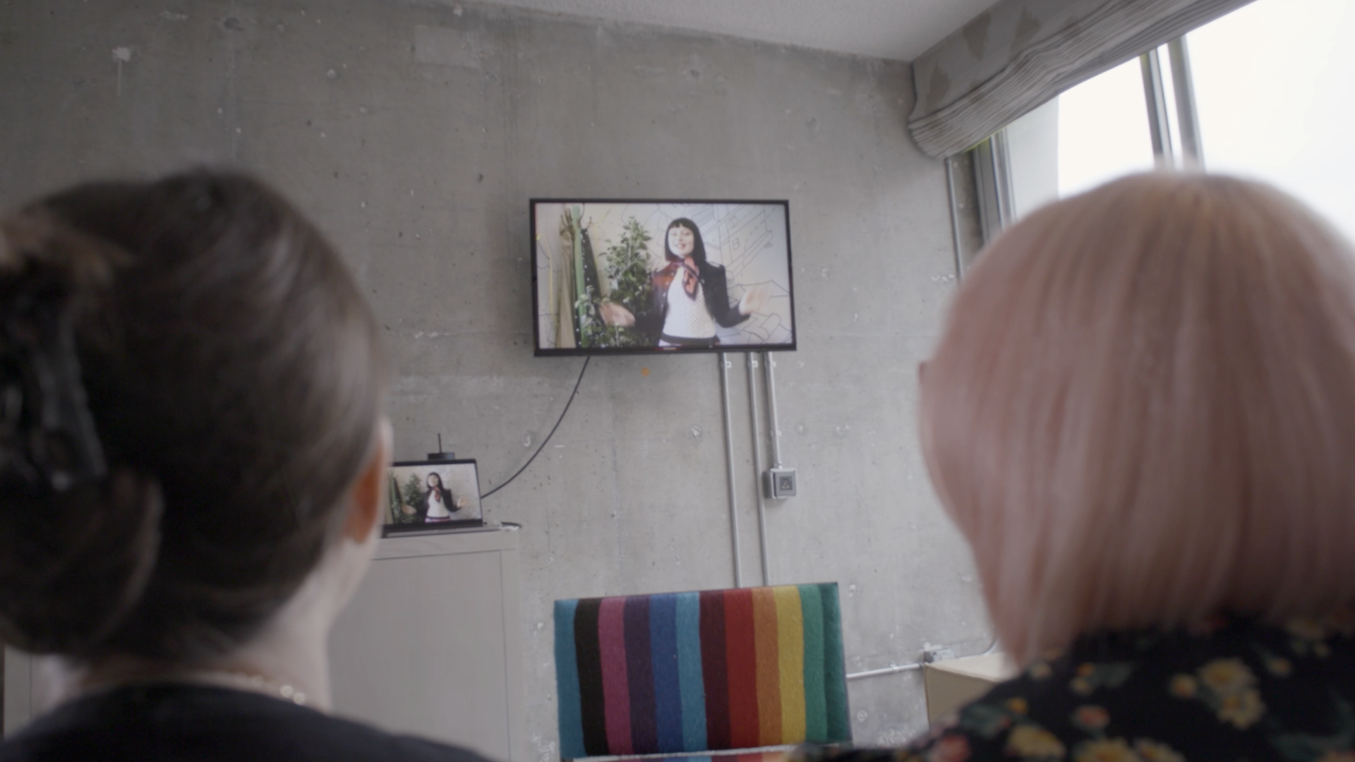 Two people watching a woman on a tv screen in a modern room.